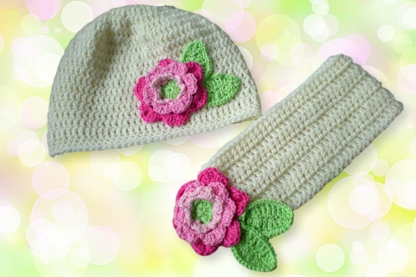 Cremefarbene handgehäkelte Babymütze und Stulpen mit rosa-pinker Blüte und grünen Blättern