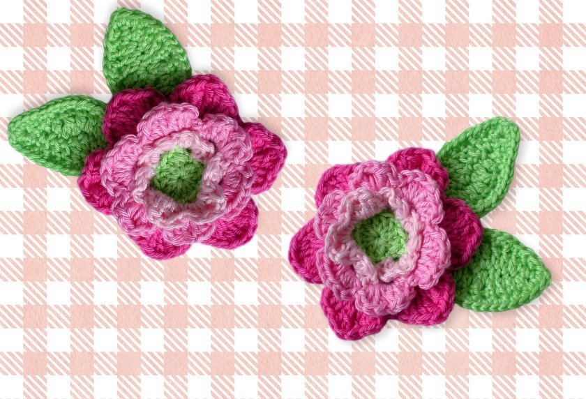 Zwei gehäkelte Blumenapplikationen in Pink und Grün auf kariertem Hintergrund