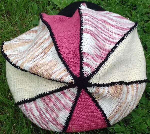 Gehäkelte Baskenmütze in Rosa, Creme und Pastell mit schwarzer Kontrastnaht, auf Gras liegend.