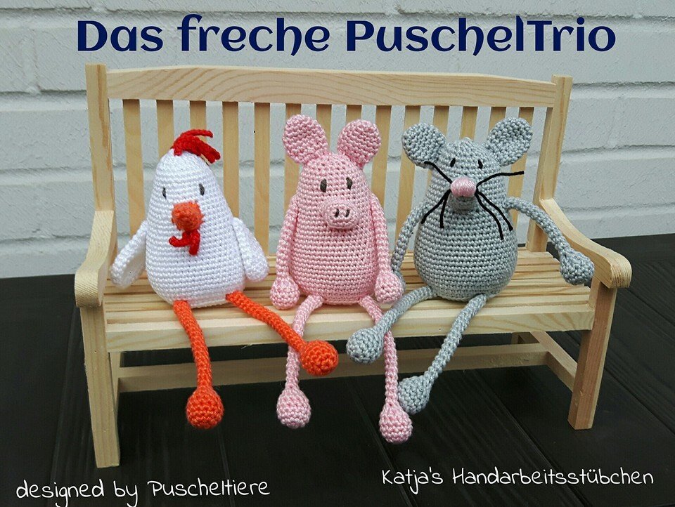Drei gehäkelte Amigurumi (Huhn, Schwein, Maus) auf einer kleinen Holzbank