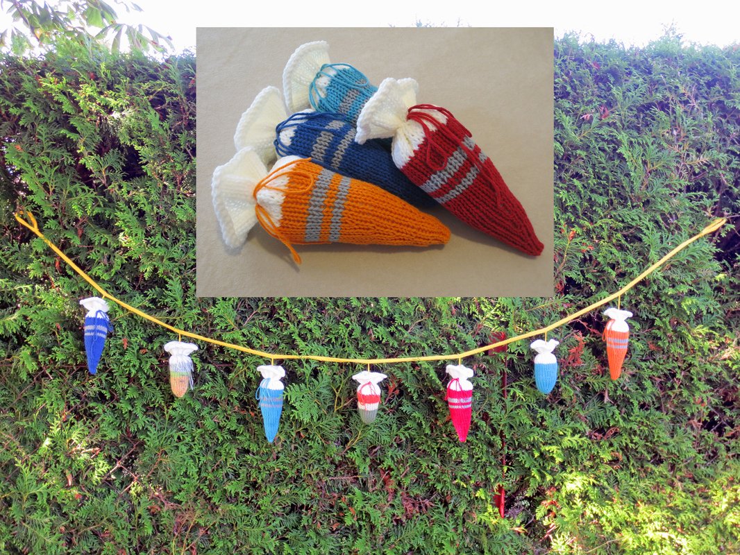 Gestrickte Mini‑Schultüten in verschiedenen Farben an einer gelben Kordel vor einer grünen Hecke; Detailaufnahme mit drei liegenden Tütchen