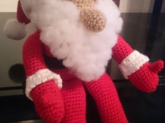 Gehäkelter sitzender Amigurumi-Weihnachtsmann mit rotem Anzug und weißem Bart