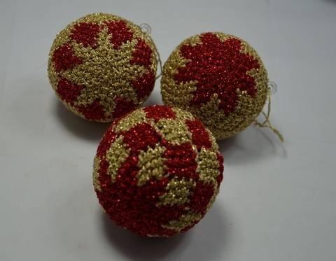Drei gehäkelte Kugeln in Rot und Gold mit sternförmigem Muster auf hellem Untergrund.
