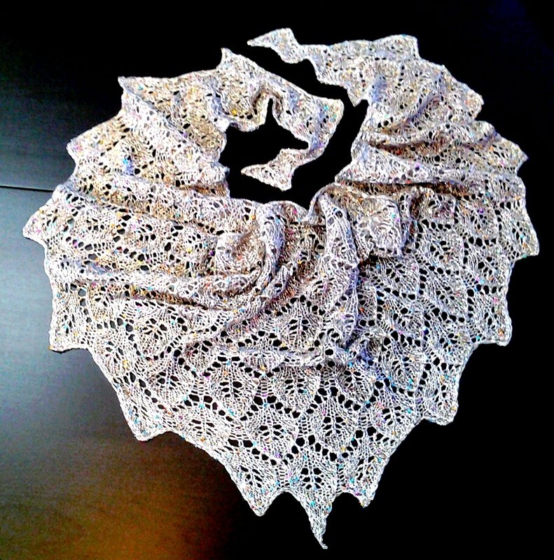 Hellgraues Spitzentuch mit Blatt‑Lochmuster und dezenten farbigen Einsprengseln auf dunklem Untergrund