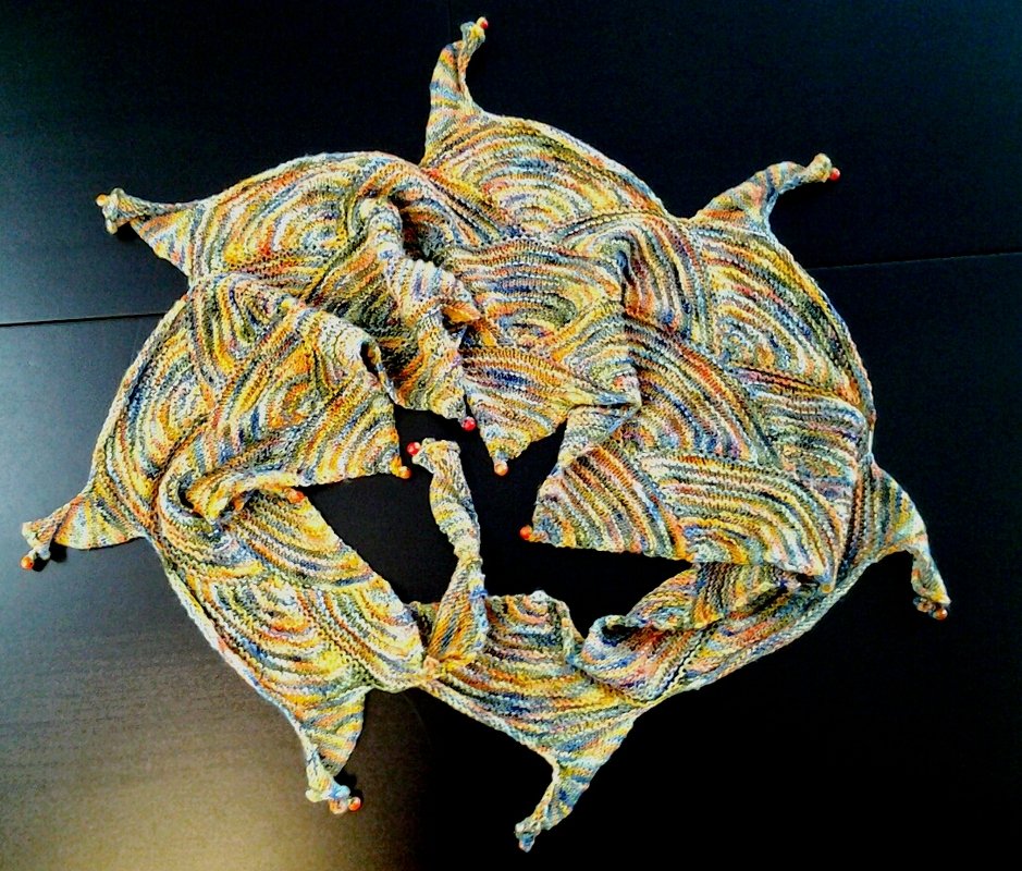 Mehrere bunte, gestrickte Dreieckstücher mit spitzen Zipfeln und Perlen, kreisförmig angeordnet