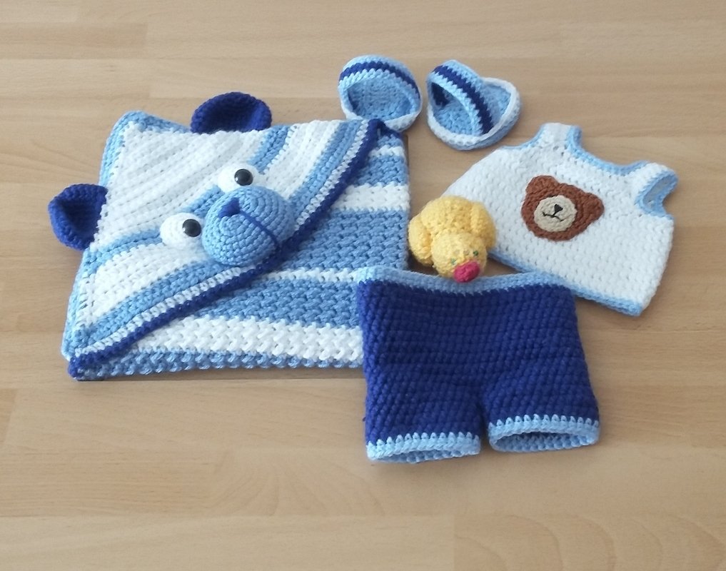 Gehäkeltes blau-weißes Babyset: Decke mit Bärenkapuze, Oberteil mit Bärenapplikation, Shorts, Schühchen und kleine gelbe Amigurumi-Ente.