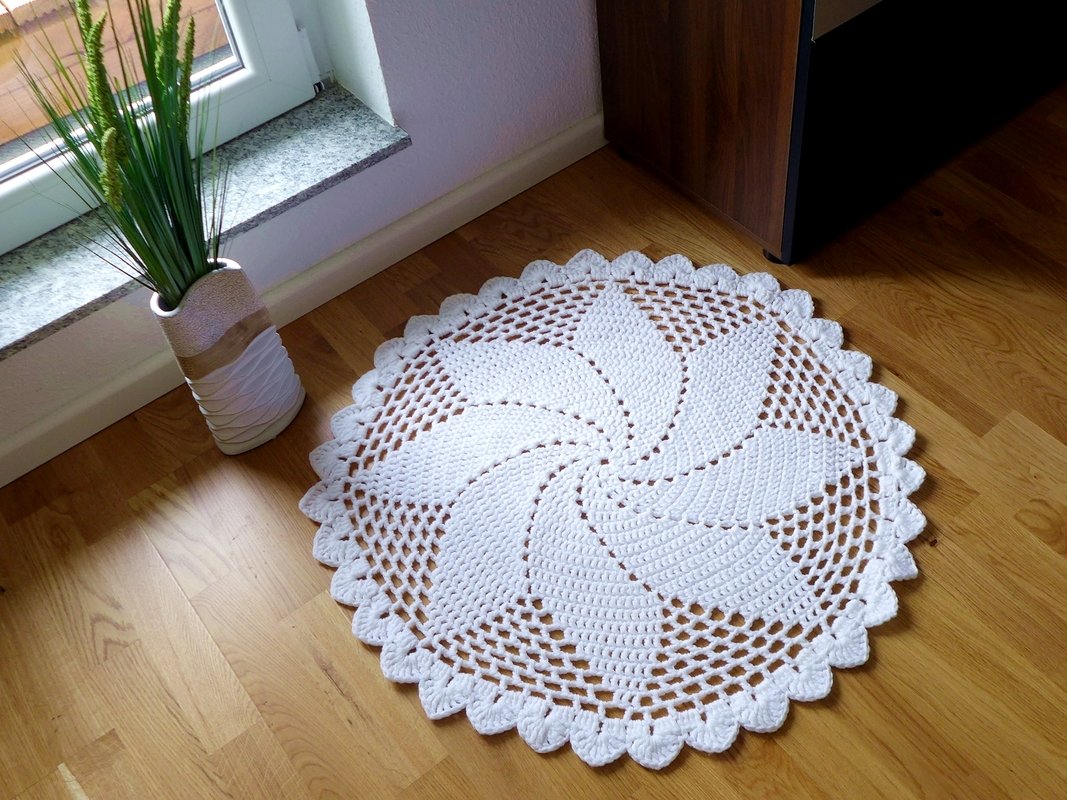Runder weißer Häkelteppich mit Spiralmuster auf hellem Holzboden