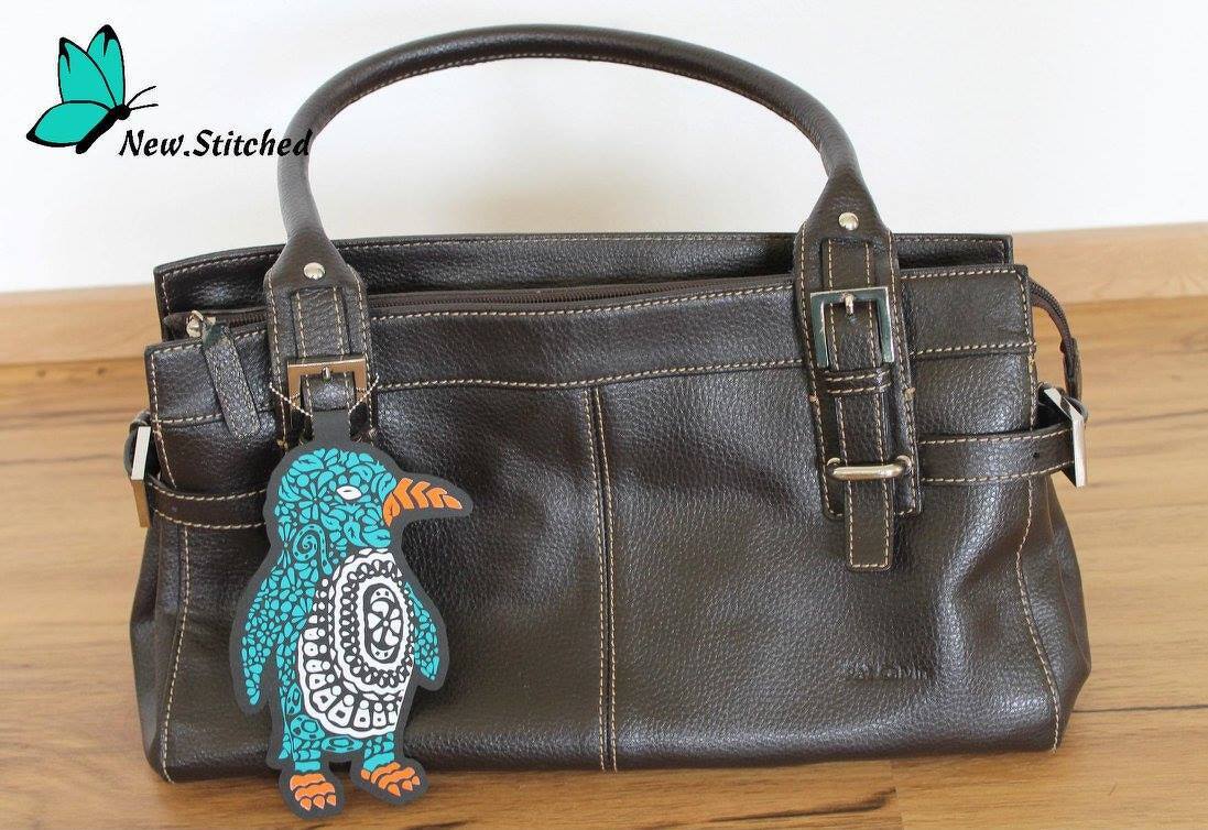 Türkis-oranger Pinguin-Anhänger mit Muster an einer braunen Handtasche