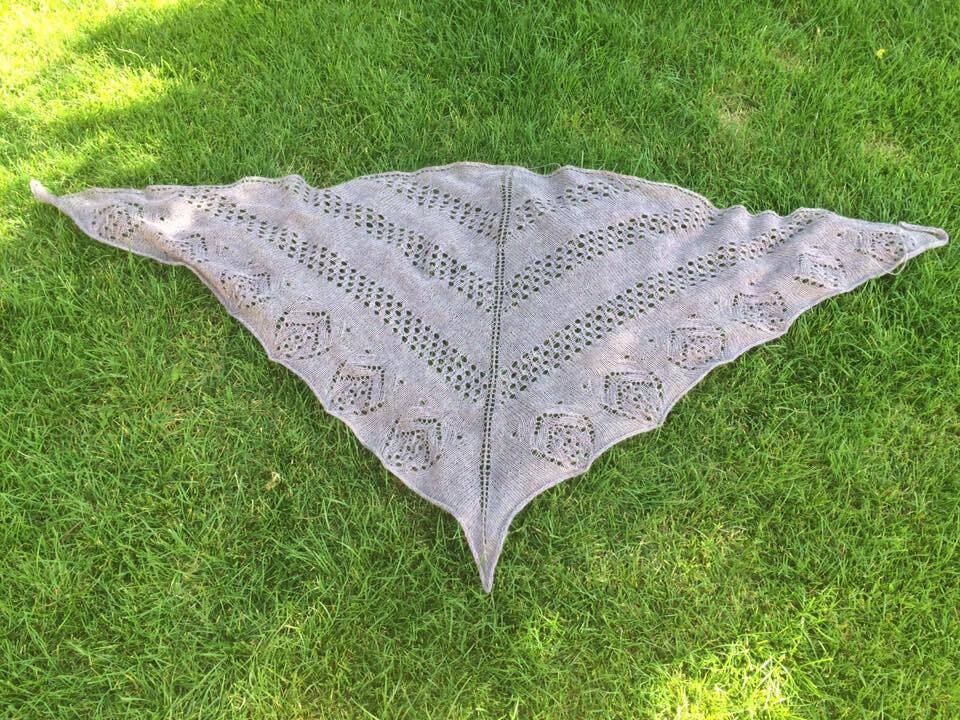 Hellgraues gestricktes Dreieckstuch mit Lochmuster und Zierkante auf grünem Rasen