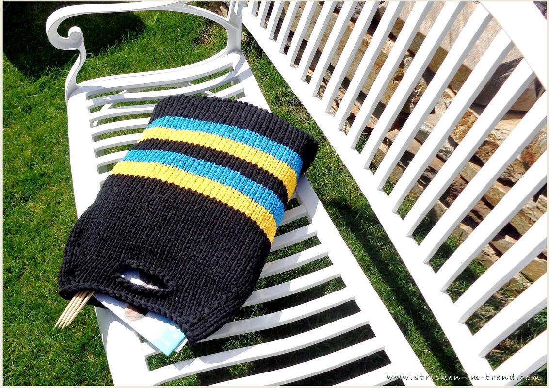Schwarze Stricktasche mit blauen und gelben Streifen auf weißer Gartenbank