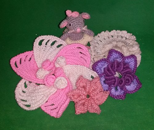 Gehäkelte Maus- und Blumenapplikationen in Rosa, Weiß und Lila auf grünem Hintergrund