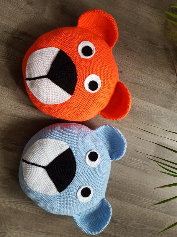 Zwei runde, gehäkelte Bärenkissen in Orange und Hellblau mit applizierter Schnauze und Augen