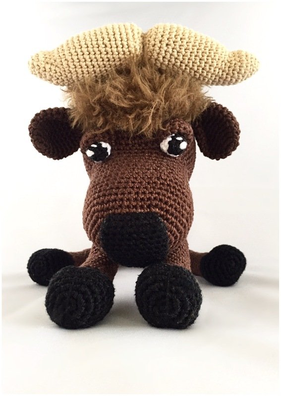 Front view of brown crochet yak amigurumi with beige horns, fluffy mane and black hooves