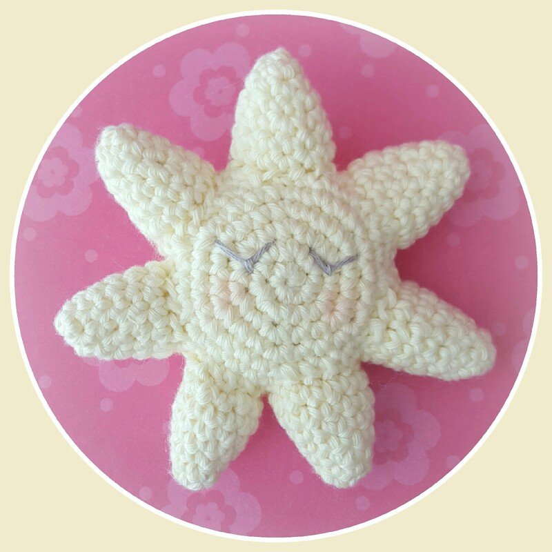 Gehäkelte kleine Sonne in Pastellgelb mit geschlossenen Augen und acht Strahlen