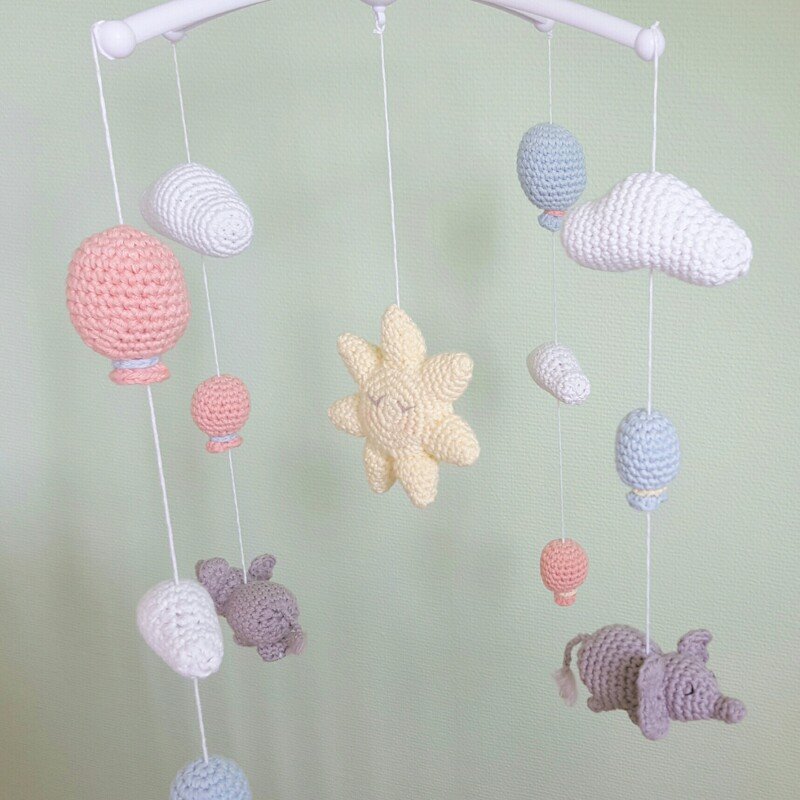Mobile mit gehäkelter Sonne, kleinen Ballons, Wolken und Elefanten vor hellgrünem Hintergrund