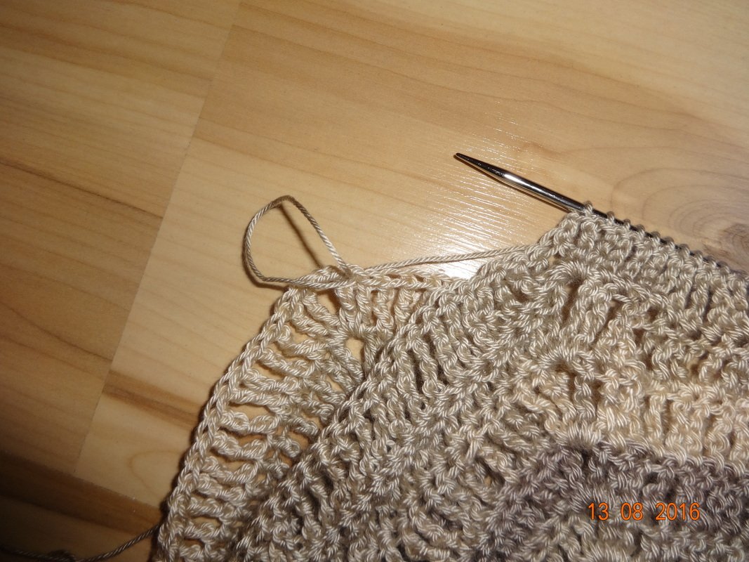 Halbfertiges gehäkeltes Textilstück in Beige mit Häkelnadel und Garn auf Holzboden.