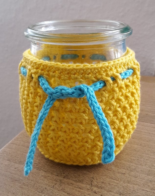 Kleines Glas mit gehäkelter Hülle und eingezogenem blauen Kordelzug