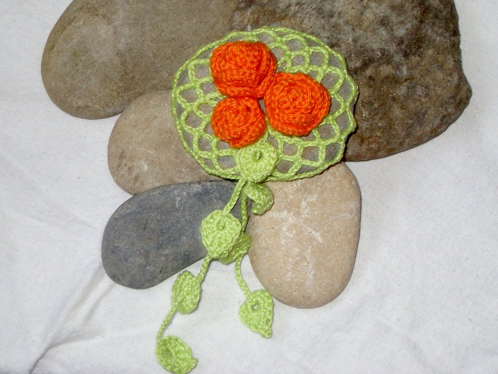 Gehäkelte Blumenapplikation mit drei orangefarbenen Rosetten auf hellgrünem Netz