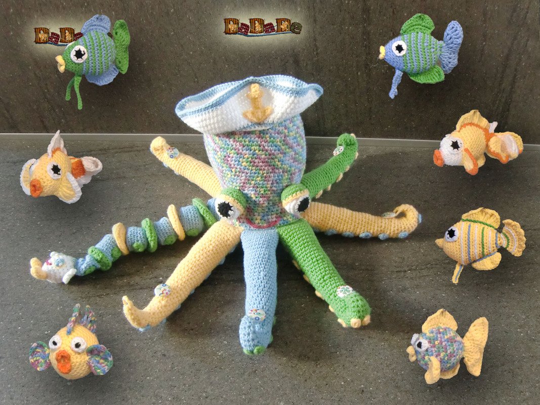 Gehäkelter Oktopus mit Matrosenhut, umgeben von bunten gehäkelten Fischen