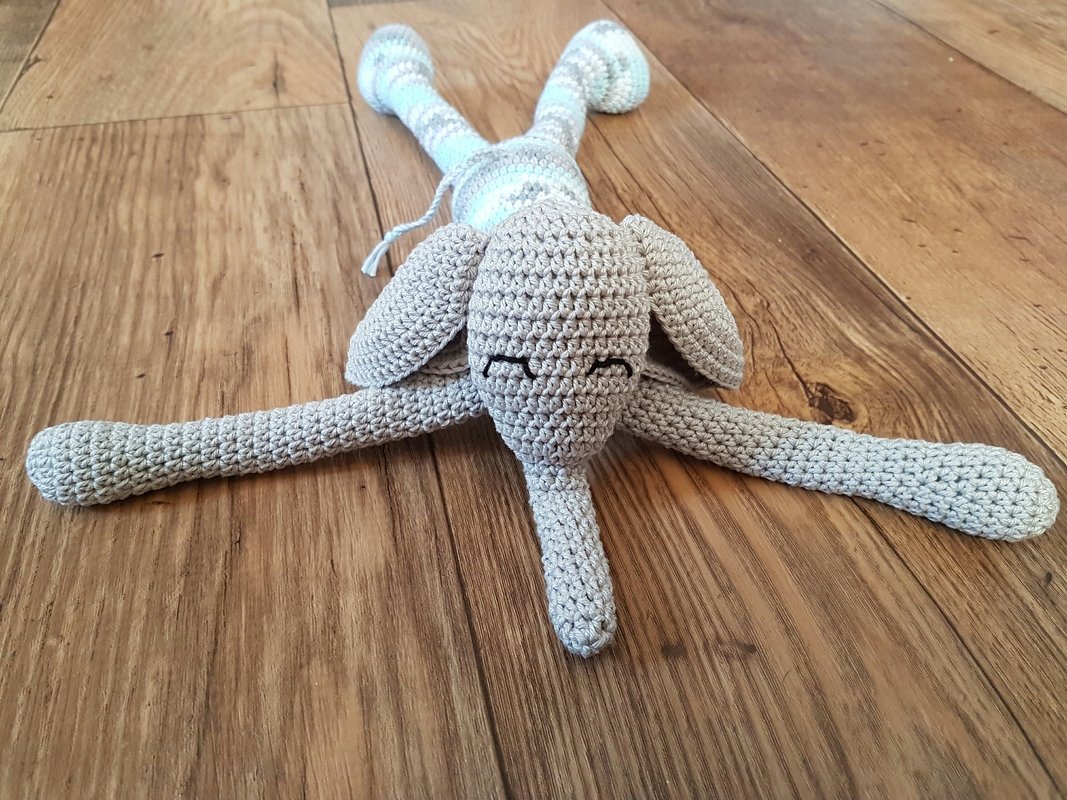 Gehäkelter grauer Amigurumi-Elefant mit hellblau-weißen Streifen auf Holzboden