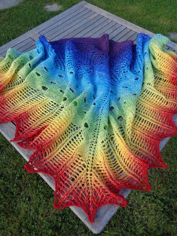 Gestricktes Dreieckstuch in Regenbogenverlauf mit Lochmuster und gezacktem Rand auf Holztisch