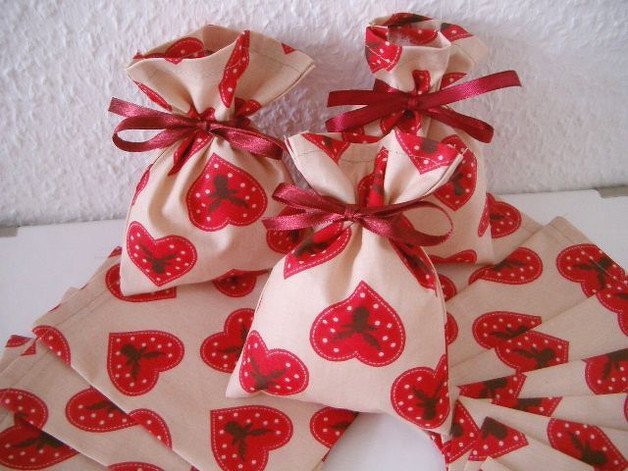 Drei genähte Stoffbeutel mit roten Herzen, oben mit rotem Satinband zugebunden, daneben passende Stoffzuschnitte