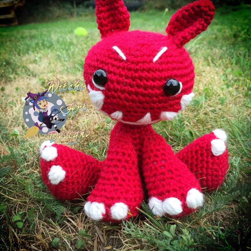 Rotes gehäkeltes Amigurumi mit weißen Akzenten im Gras