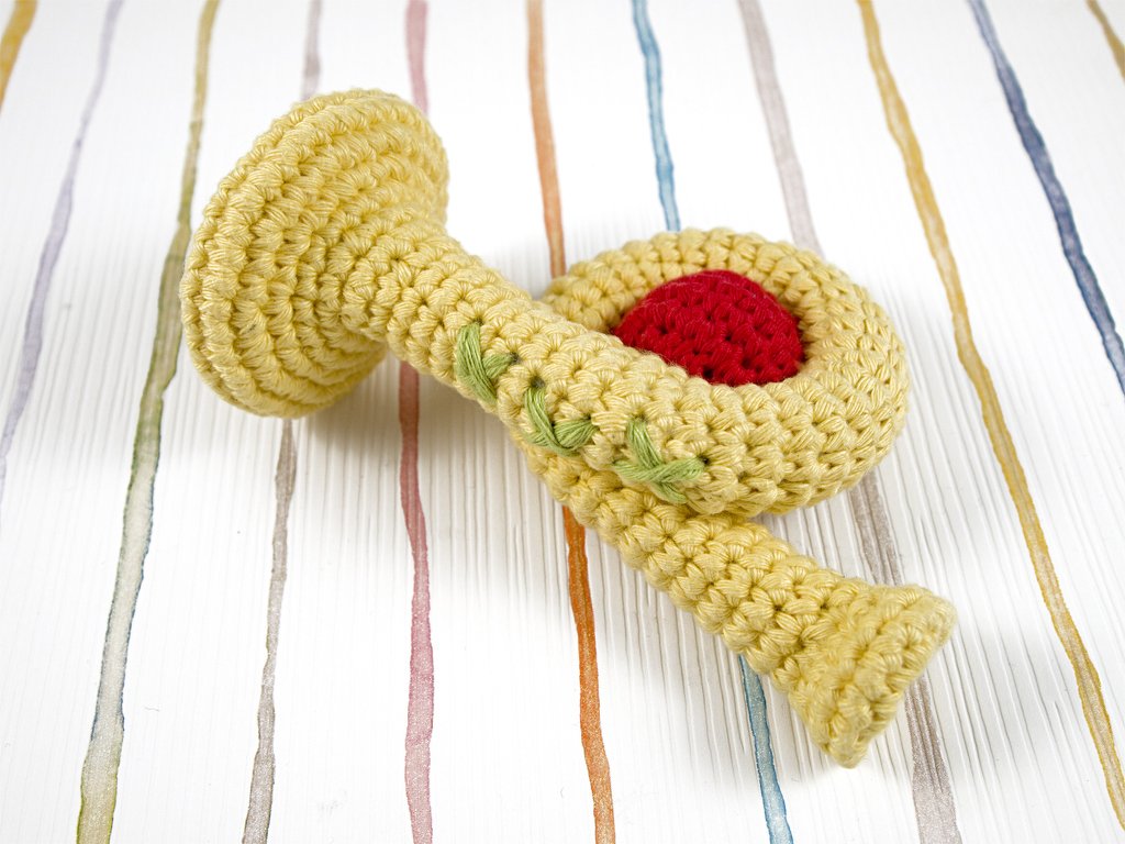 Gehäkelte gelbe Rassel in Trompetenform mit rotem Einsatz und grünen Stickdetails