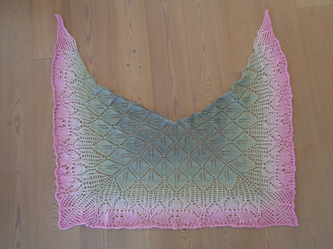 Dreieckstuch mit Blatt-Lochmuster und Farbverlauf von Rosa zu Grün auf Holzboden.