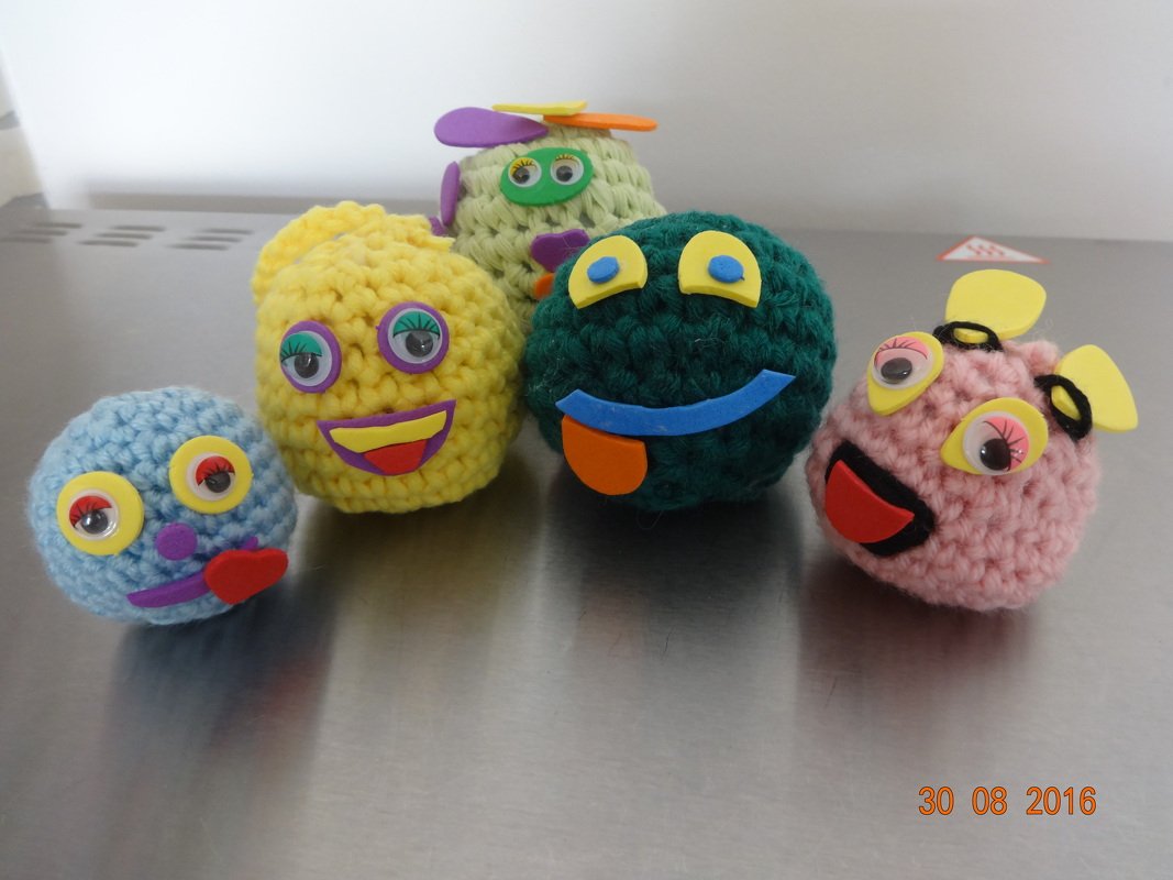 Fünf bunte gehäkelte Amigurumi‑Figuren mit Wackelaugen auf einer Metallfläche
