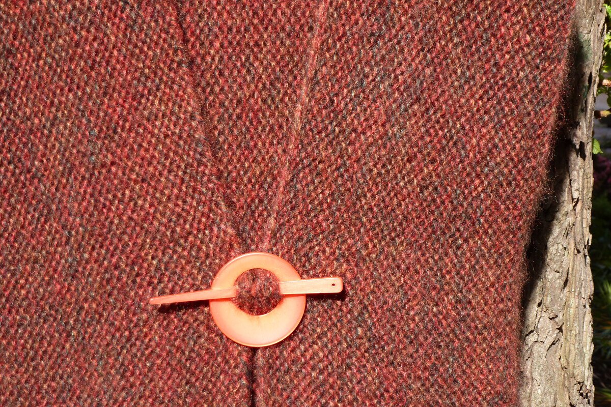 Nahaufnahme einer rostroten gestrickten Jacke mit rundem orangen Schließring