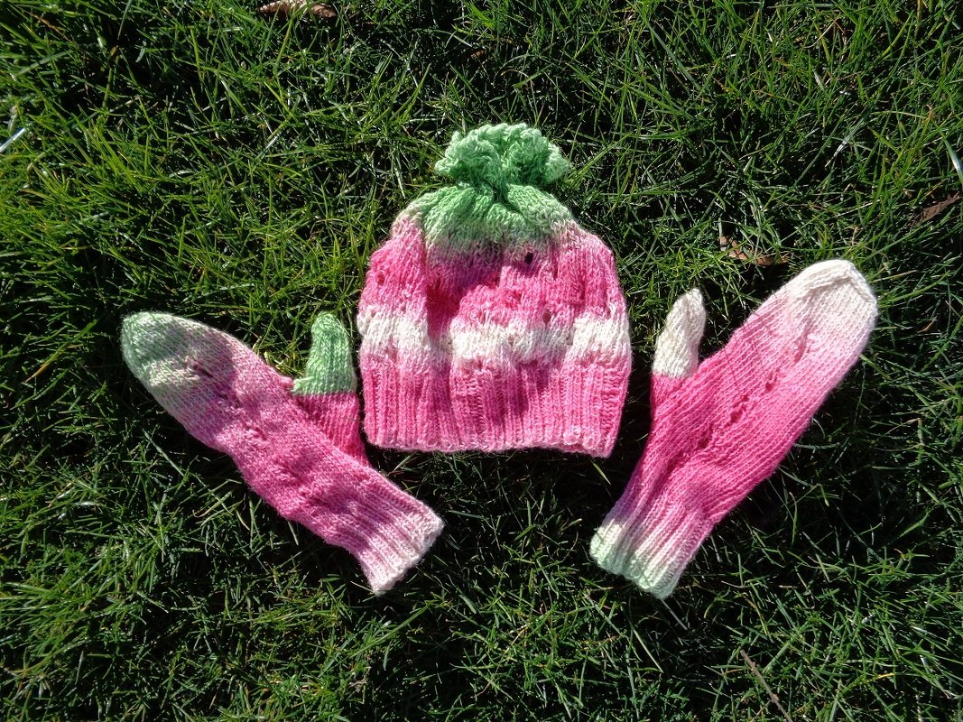 Gestricktes Mützen- und Fäustlings-Set in Rosa, Weiß und Grün auf Gras