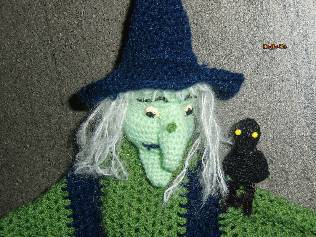 Gehäkelte Hexe mit grünem Gesicht, blauem Hut und kleinem schwarzem Raben