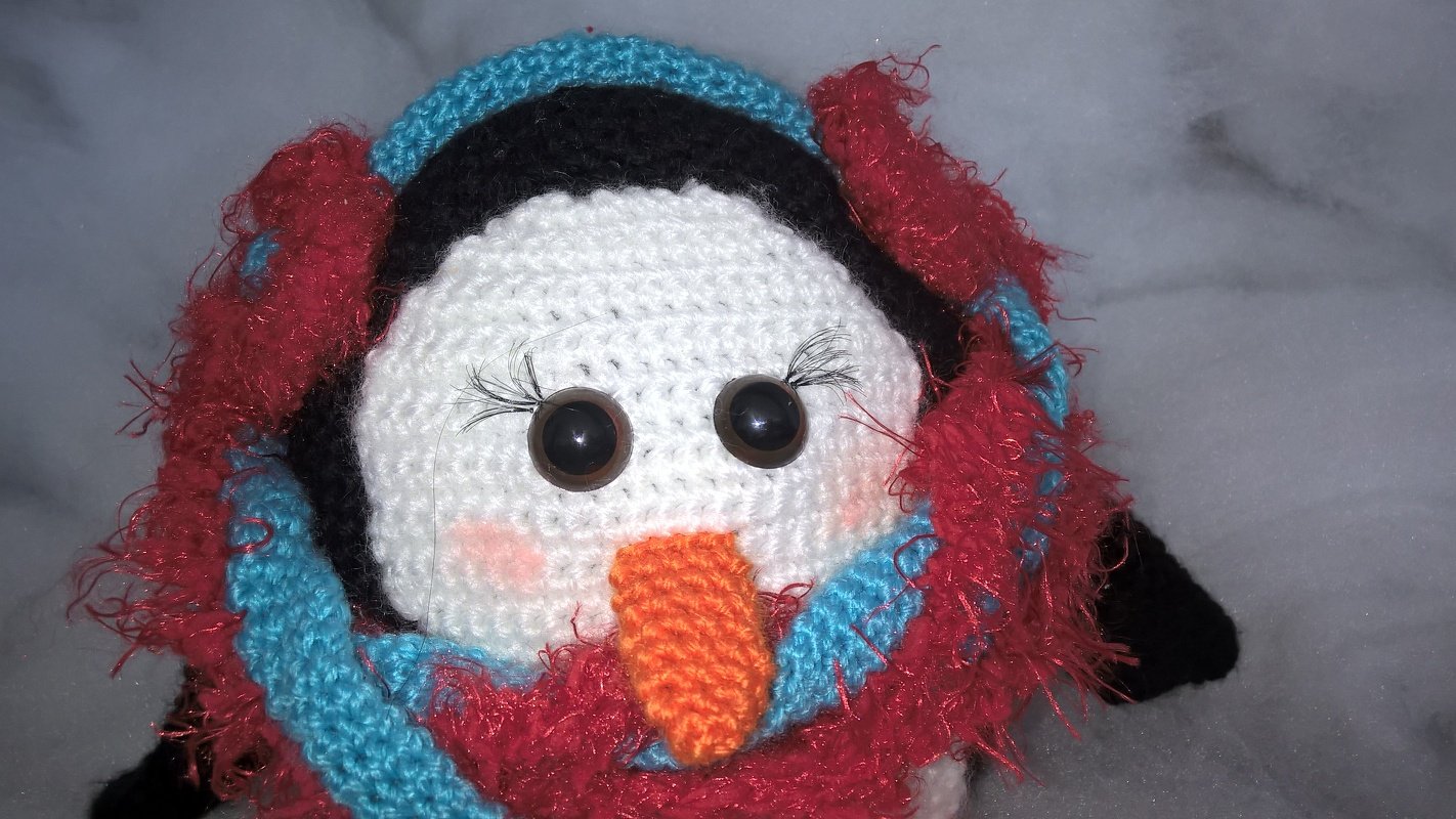 Weihnachtlicher Amigurumi Pinguin mit roten flauschigen Ohrenschützern und blau gestreiftem Schal