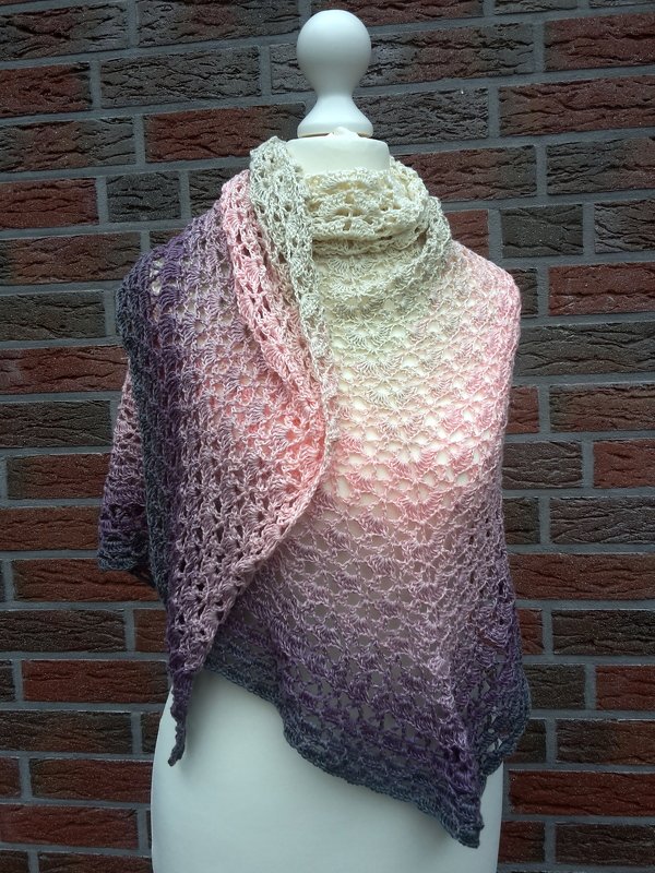Gehäkeltes Dreieckstuch mit Farbverlauf von Creme über Rosa zu Violett auf Schaufensterpuppe vor Backsteinwand