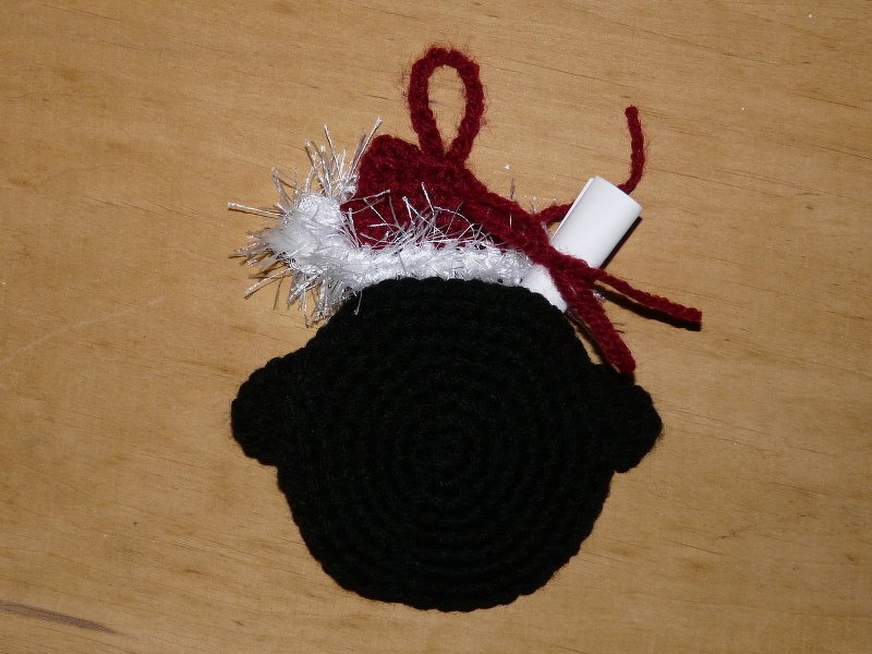 Gehäkelter schwarzer Kreis mit roter Weihnachtsmütze und Aufhängeschlaufe