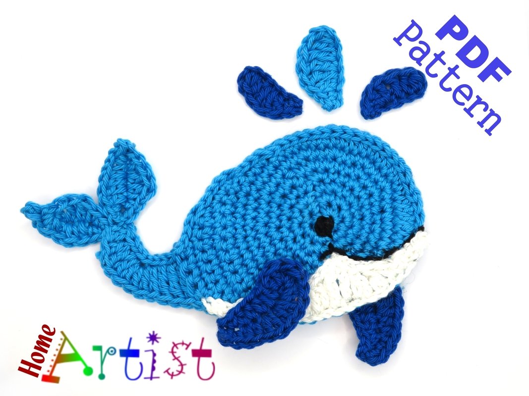 Flat blue crocheted whale applique with white belly and dark blue fins on white background