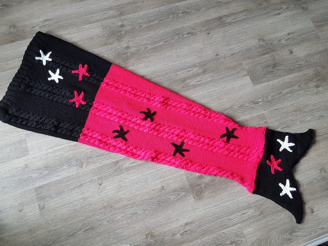 Gestrickte Meerjungfrauendecke in Pink und Schwarz mit Zopfmuster und Sternapplikationen auf hellem Holzfußboden