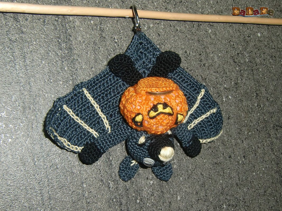 Gehäkelter Fledermaus-Schlüsselanhänger in Dunkelblau mit orangefarbenem Kürbiskopf, an einer Stange aufgehängt