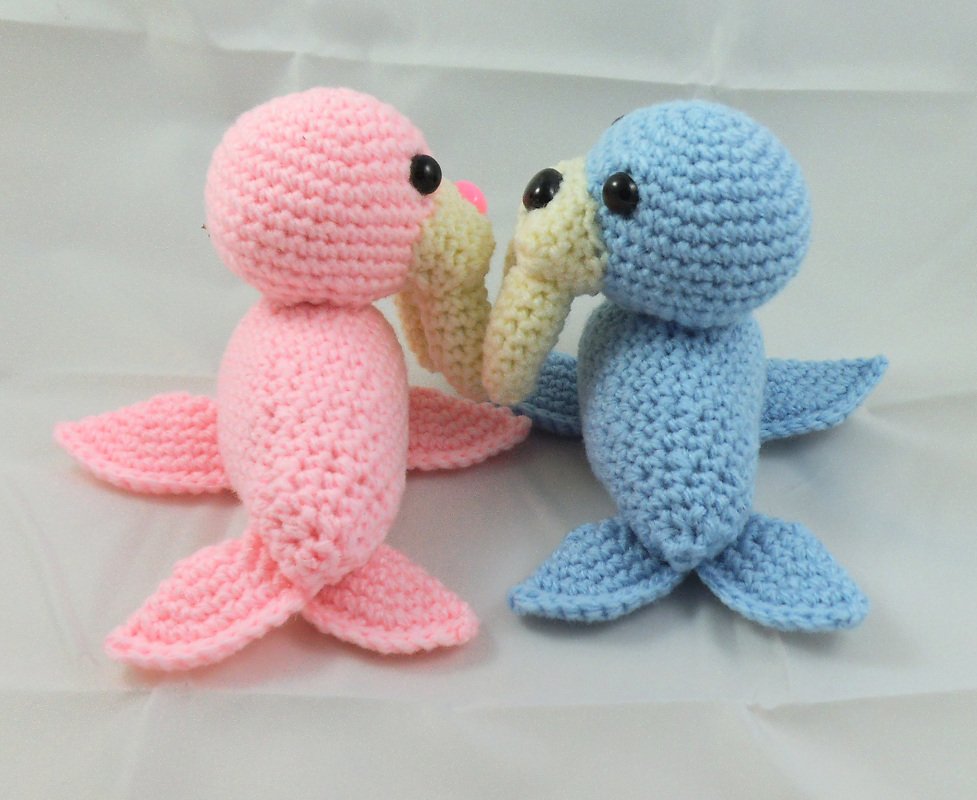 Rosa und blaue gehäkelte Amigurumi-Robben mit beigefarbenen Schnauzen und schwarzen Augen, einander zugewandt