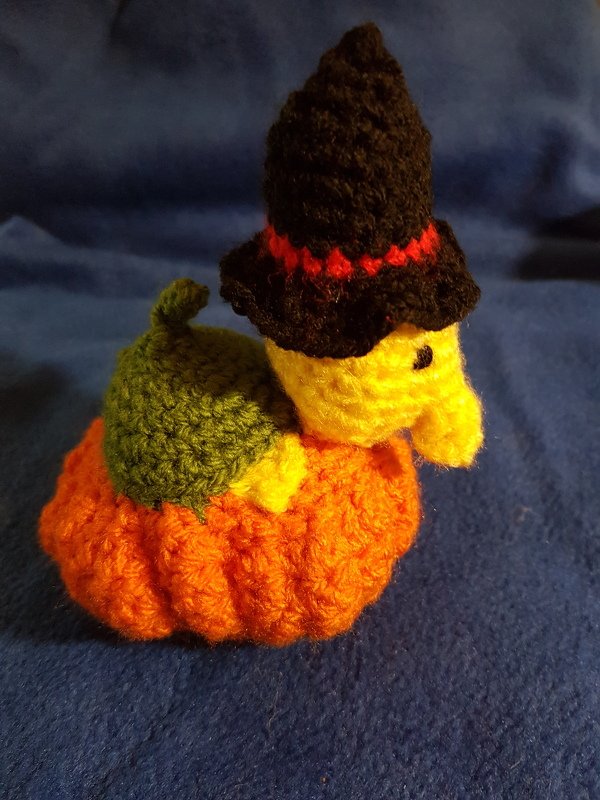 Mini-Amigurumi: gelbes Küken mit schwarzem Hexenhut auf orangefarbenem Kürbis