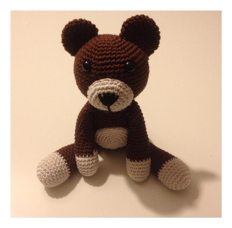Sitzender brauner Amigurumi-Teddybär mit heller Schnauze, Bauch und Pfoten vor hellem Hintergrund.