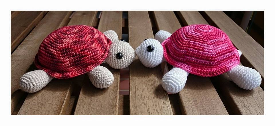 Zwei gehäkelte Amigurumi-Schildkröten mit rot- und pink-melierten Panzern auf Holz.
