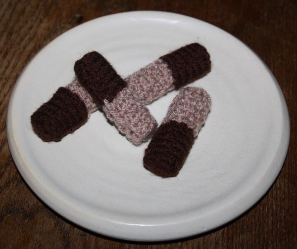 Drei gestrickte kleine Zylinder aus braunem und beigem Garn auf weißem Teller