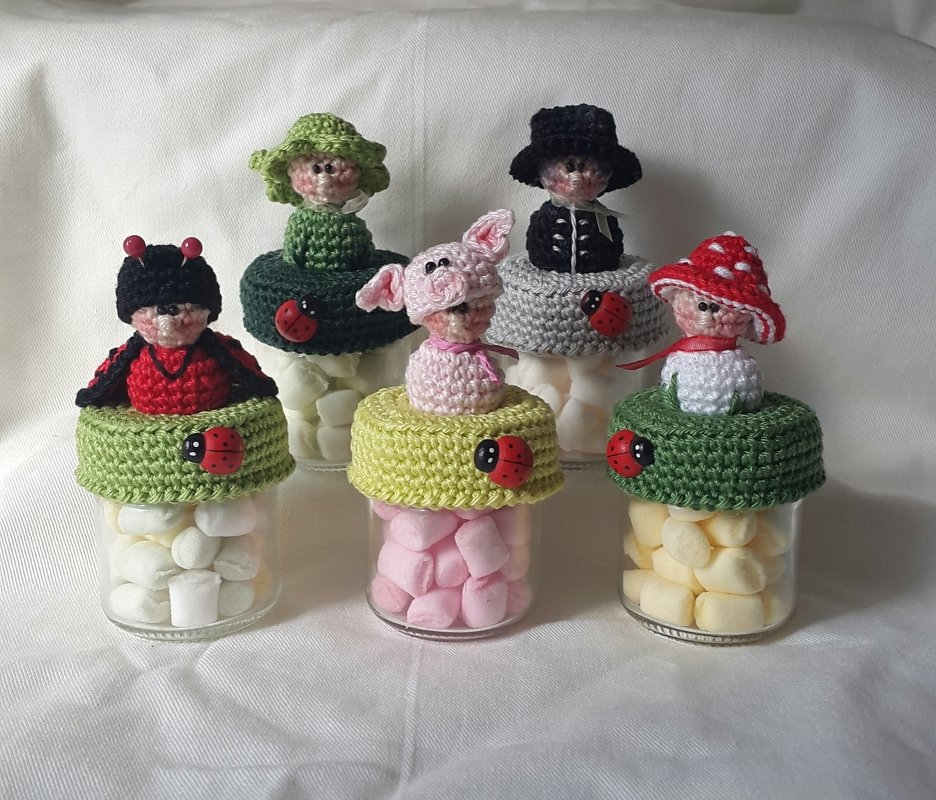 Fünf Gläser mit Schaumzucker und gehäkelten Glücksbringer-Figuren auf den Deckeln