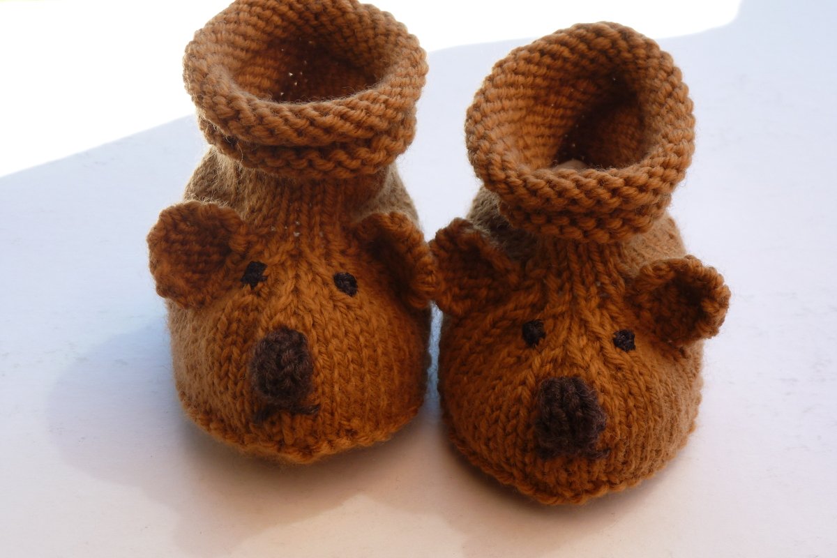 Zwei braune, gestrickte Babyschuhe mit Bärengesichtern auf weißem Untergrund