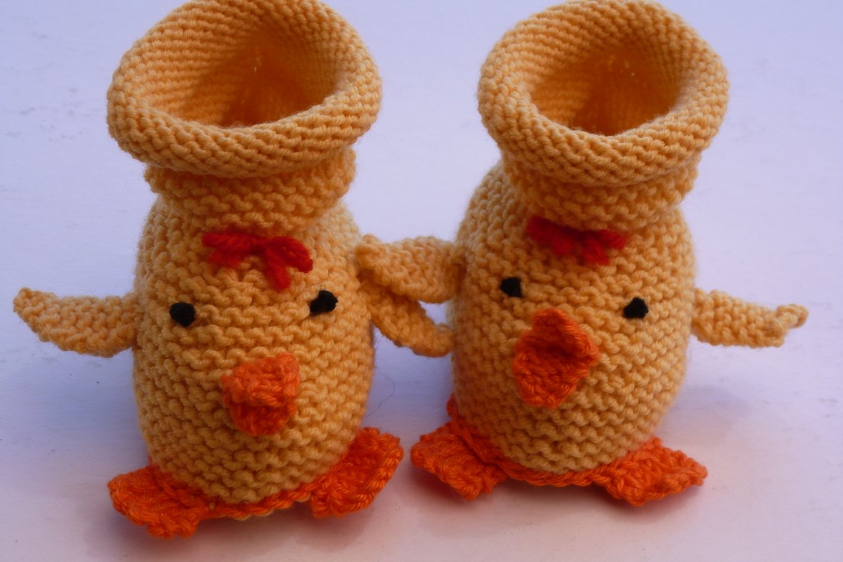 Zwei gelb-orangene, gestrickte Babyschuhe in Kükenform mit umgeschlagenem Bund, kraus rechts gearbeitet.