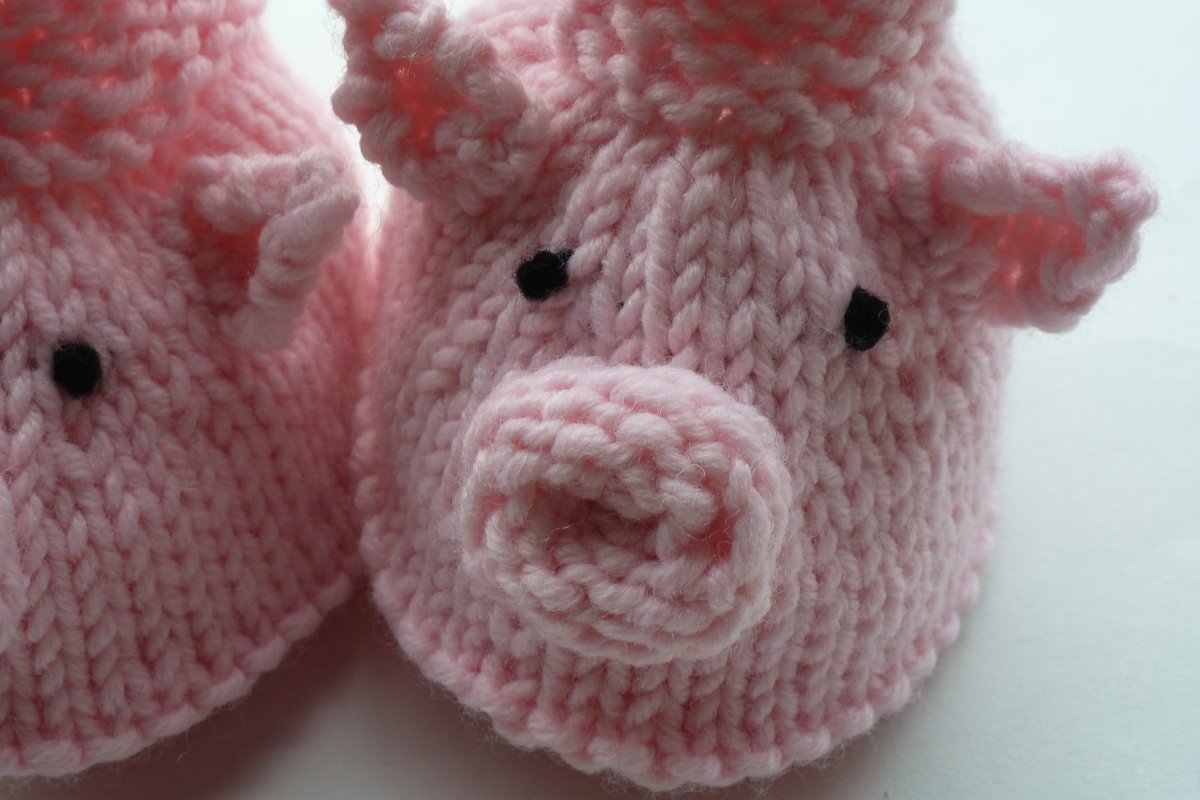 Nahaufnahme eines rosa gestrickten Babyschuhs mit aufgesetzter Schnauze und schwarzen Augen