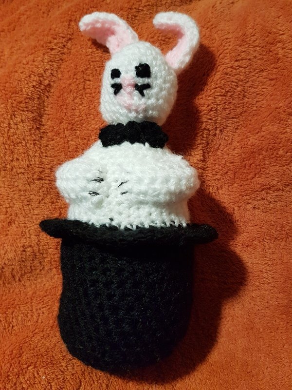 Amigurumi-Hase mit rosa Ohren im schwarzen Zylinder auf orangefarbenem Stoff