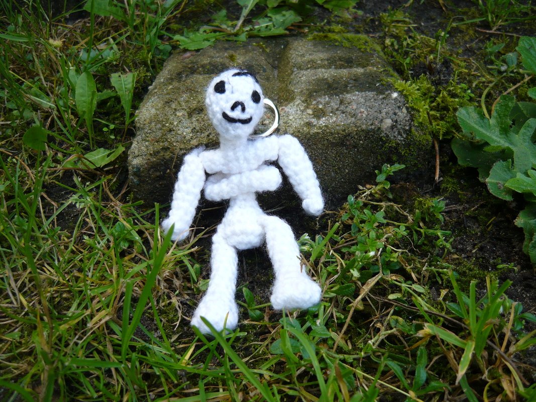 Gehäkelter weißer Skelett-Schlüsselanhänger auf Gras vor einem Stein